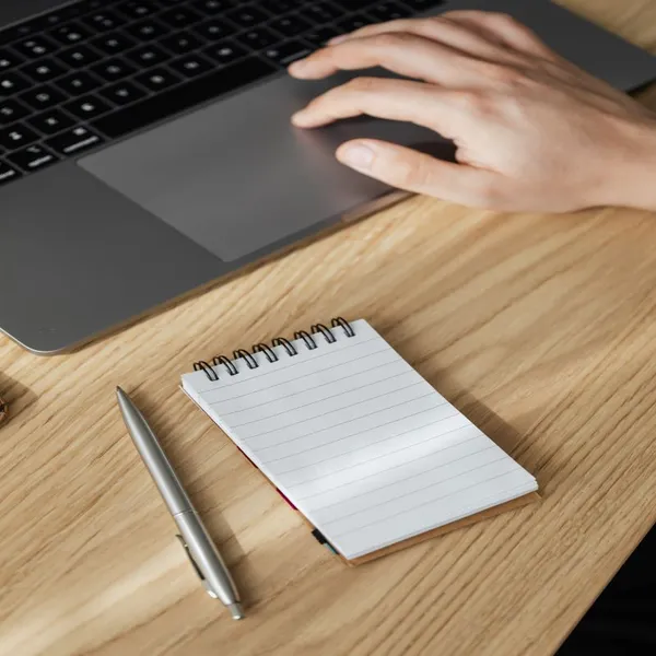 Image d'un homme assis à son bureau main sur l'ordinateur portable, un bloc note papier et un stylo